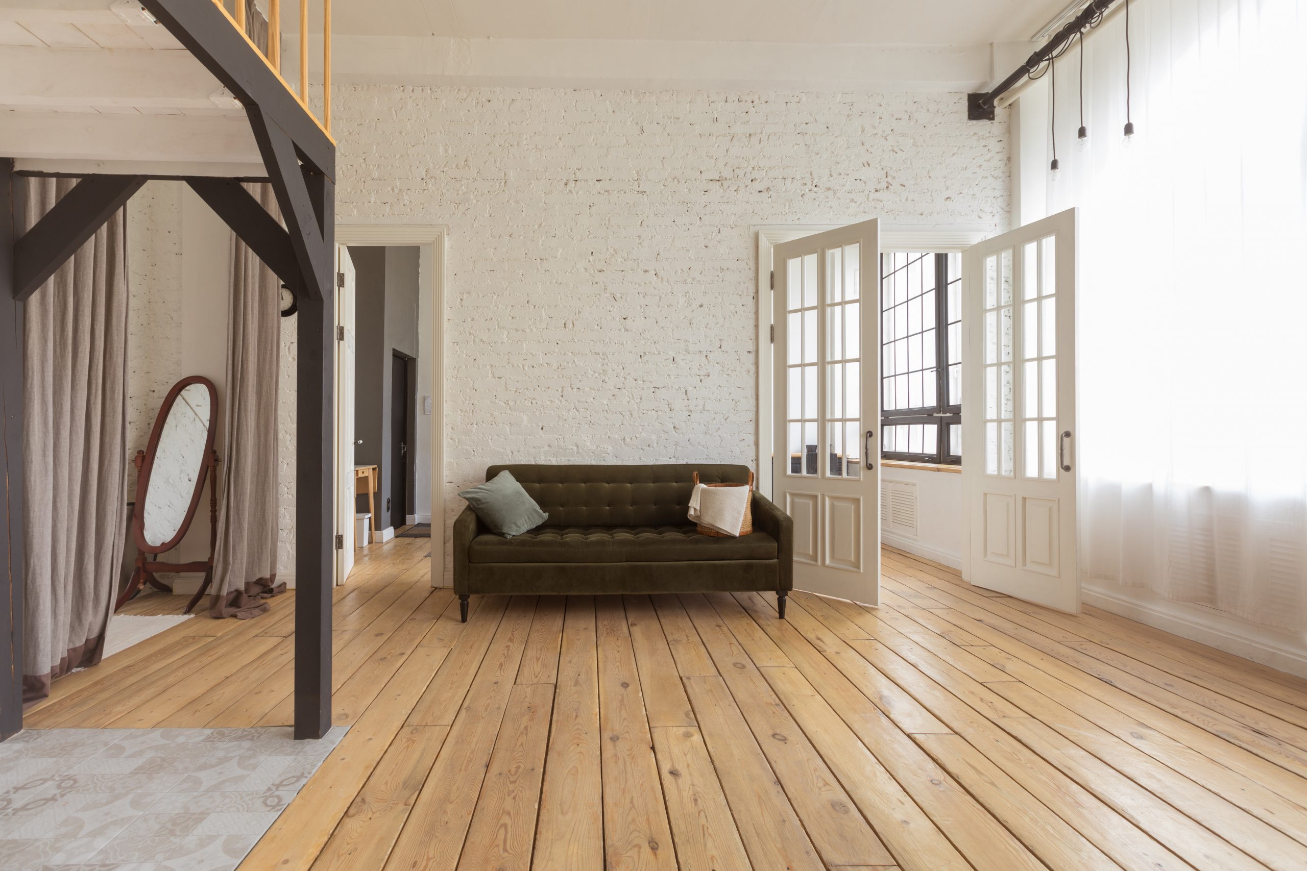 Comfortable sofa located near open doors in spacious room of light loft flat